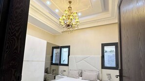 A bedroom with a large bed, two bedside tables, a chandelier, and a mirror.