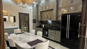 A modern kitchen with marble countertops, stainless steel appliances, and a chandelier.
