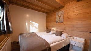 Een slaapkamer in een houten blokhut met een bed, nachtkastjes en een schilderij aan de muur.