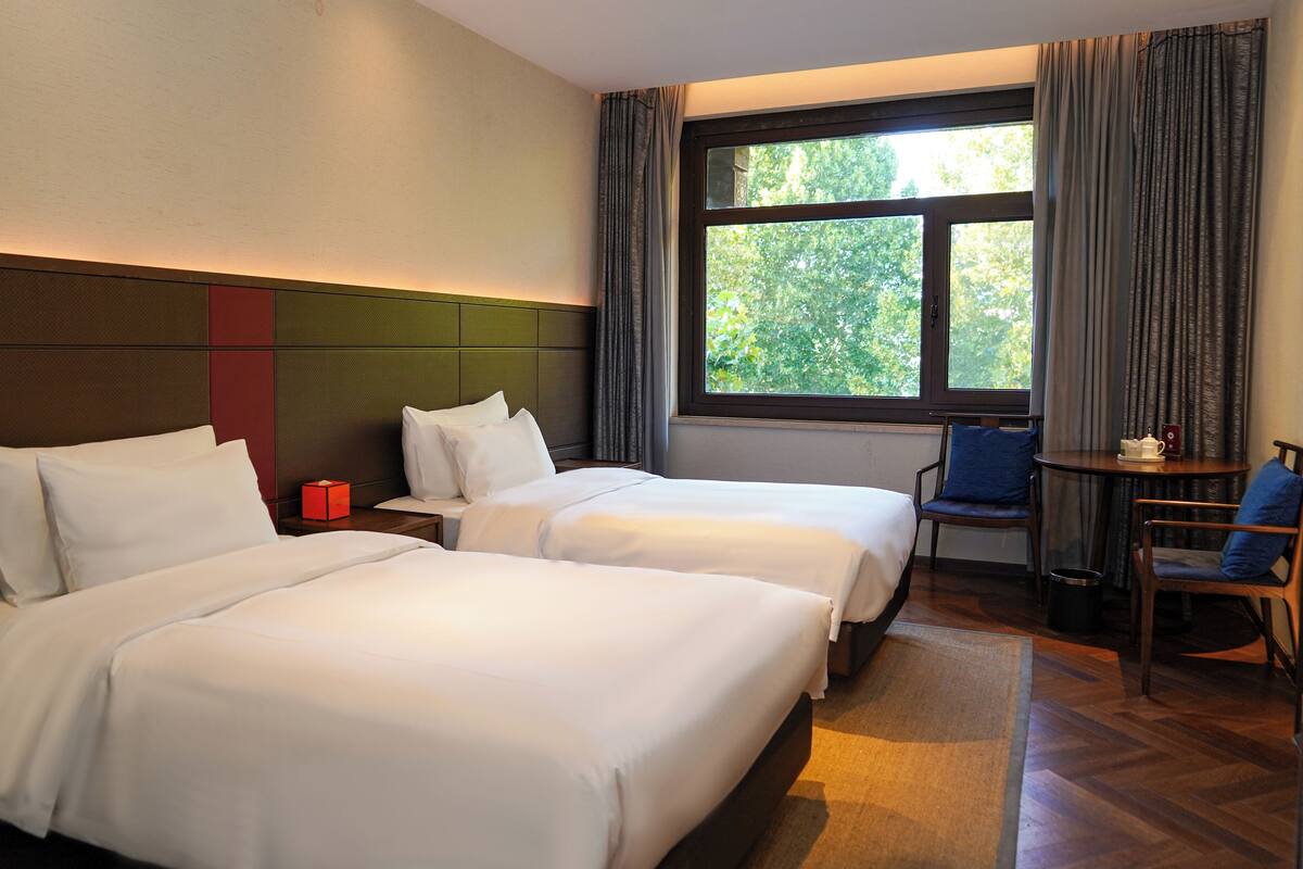Een hotelkamer met twee bedden, een tafeltje, een stoel en een raam met gordijnen.