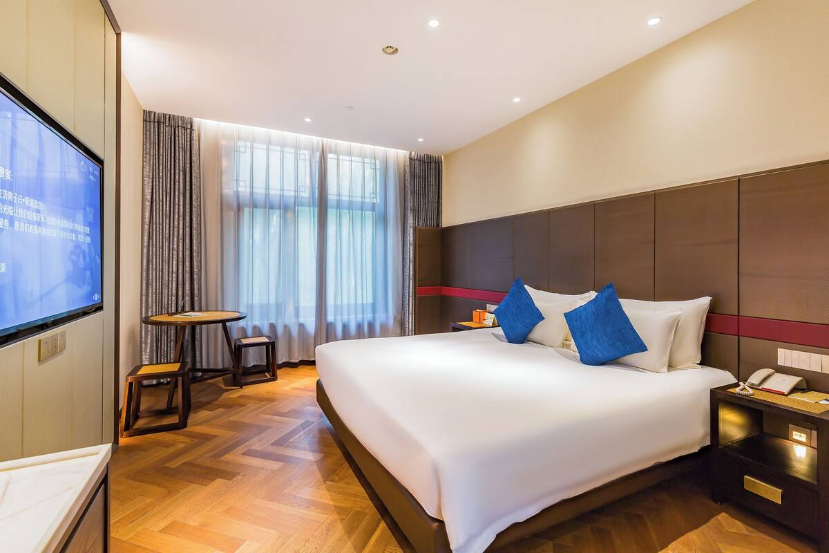 Een moderne hotelkamer met een groot bed, een nachtkastje, een klein bureau met stoel en een aan de muur bevestigde televisie.