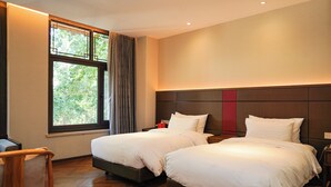 Une chambre d’hôtel avec deux lits, un plancher en bois, une fenêtre avec des rideaux et une table de chevet avec une lampe.
