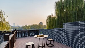 Une terrasse en bois avec une table ronde et deux tabourets, d’où l’on peut admirer une vue sur la ville et un pagode traditionnel.