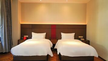 A hotel room with two beds, a large headboard, and a red accent wall.