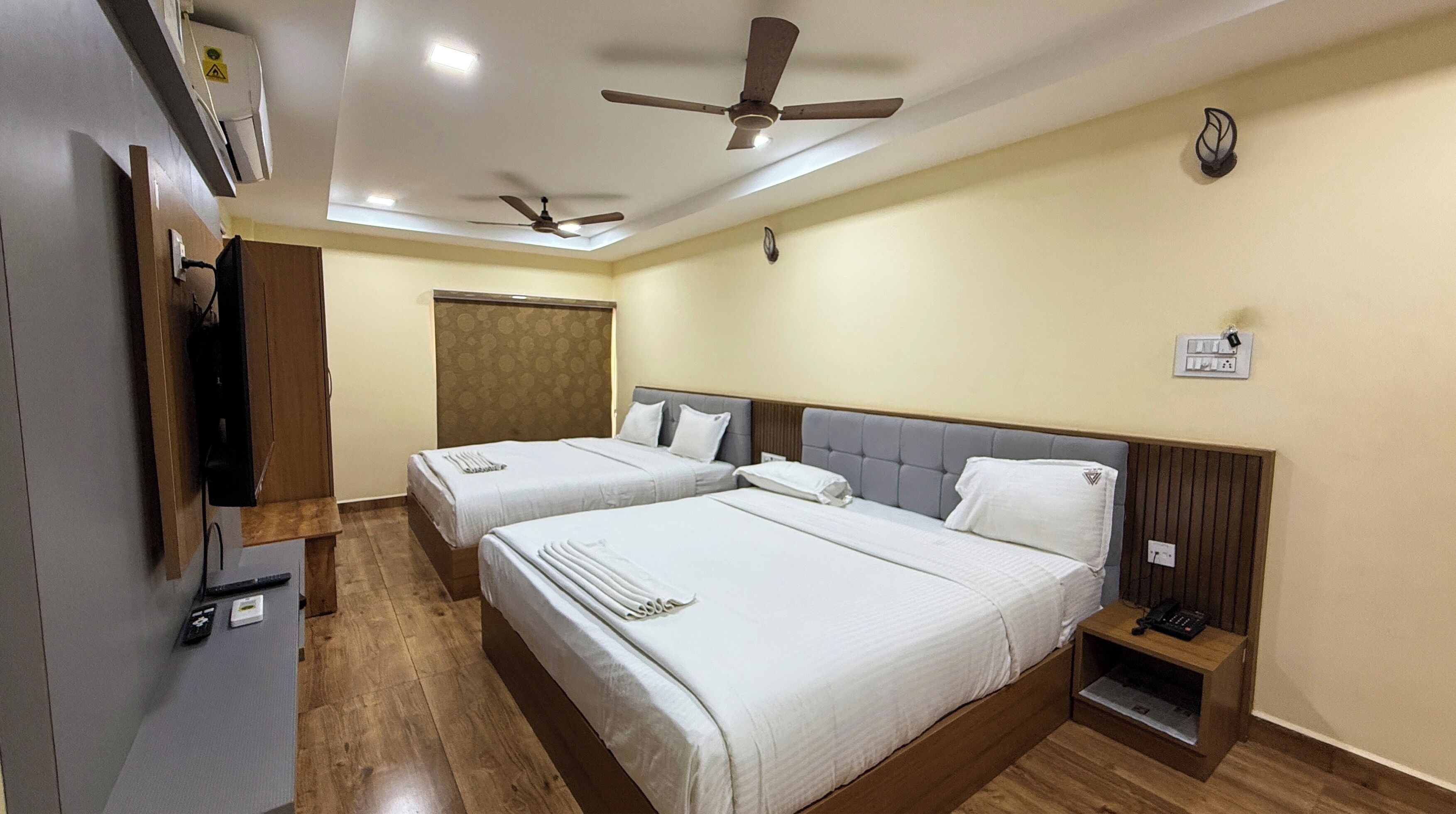 Habitación de hotel con dos camas, suelo de madera, ventiladores de techo, un armario y una mesita de noche con teléfono.