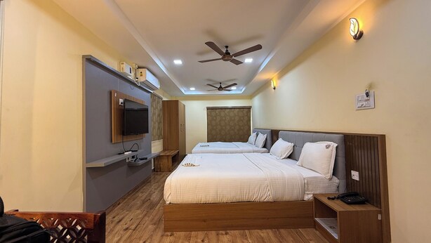 Quarto de hotel com duas camas, televisão na parede, ventiladores no teto e uma pequena mesa com telefone.