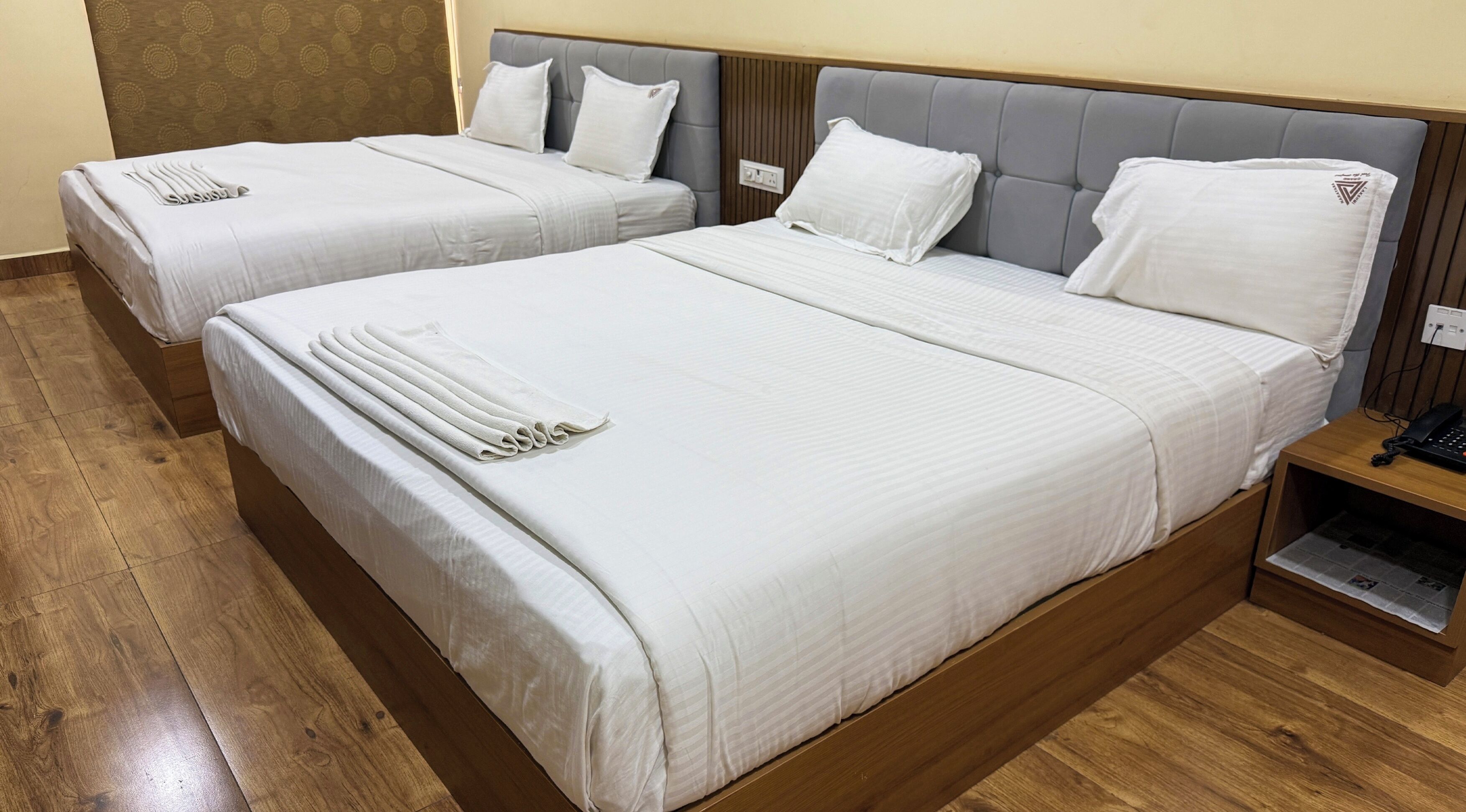 Dos camas individuales con sábanas blancas, suelo de madera y una mesita de noche con teléfono.