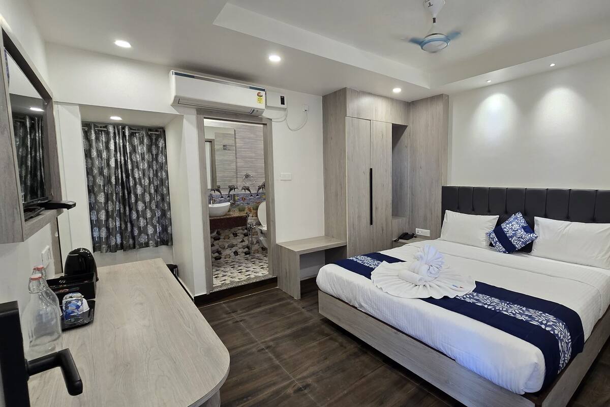 A modern hotel room with a bed, bedside table, and a bathroom visible through an open door.