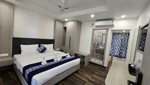 A hotel room with a bed, bedside tables, a bathroom with a sink and mirror, and a ceiling fan. - Hotel Akshaya (Port Blair)