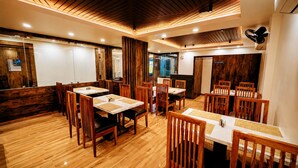 A restaurant with wooden flooring, tables with woven placemats, and a modern ceiling design. - Hotel Akshaya (Port Blair)