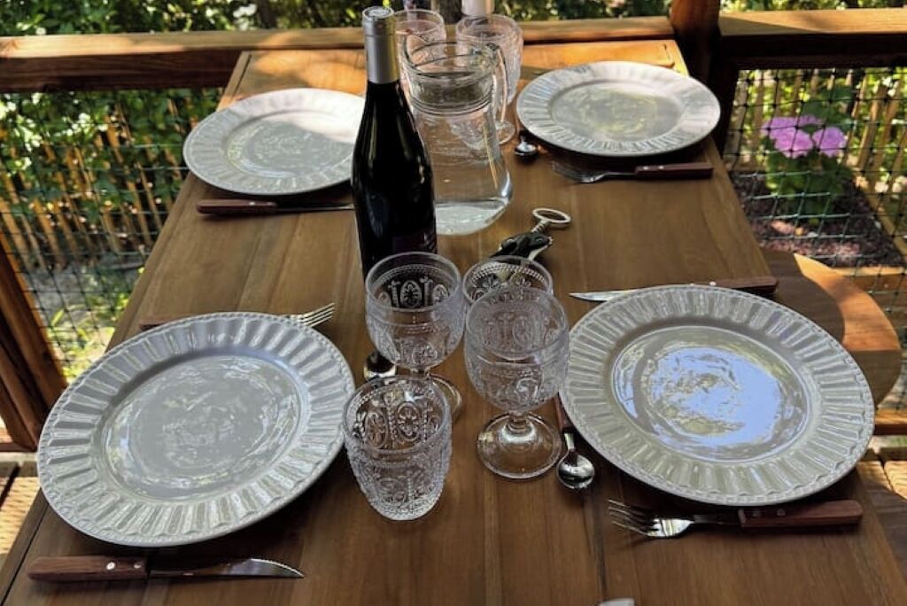 A wooden table set with plates, cutlery, and glasses, with a bottle of wine and a water glass.