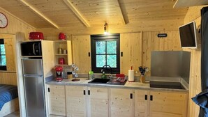 A compact wooden cabin with a kitchenette, including a refrigerator, microwave, and sink. - Comfortable wooden cabins for rent (heating & air-conditioning). (Clermont-l'Hérault)