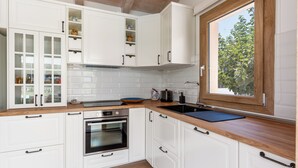 Eine moderne Küche mit weißen Schränken, einer Holz Arbeitsplatte, einem Einbauofen, einer Spüle und einem Fenster mit Blick auf Bäume.
