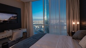 A modern hotel room with a large bed, a desk, a TV, and a view of a cityscape through large windows. - Luxury Apartment in DAMAC Towers (Riyadh)