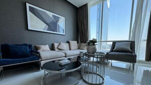 A modern living room with a sofa, a coffee table, and a view of tall buildings. - Luxury Apartment in DAMAC Towers (Riyadh)