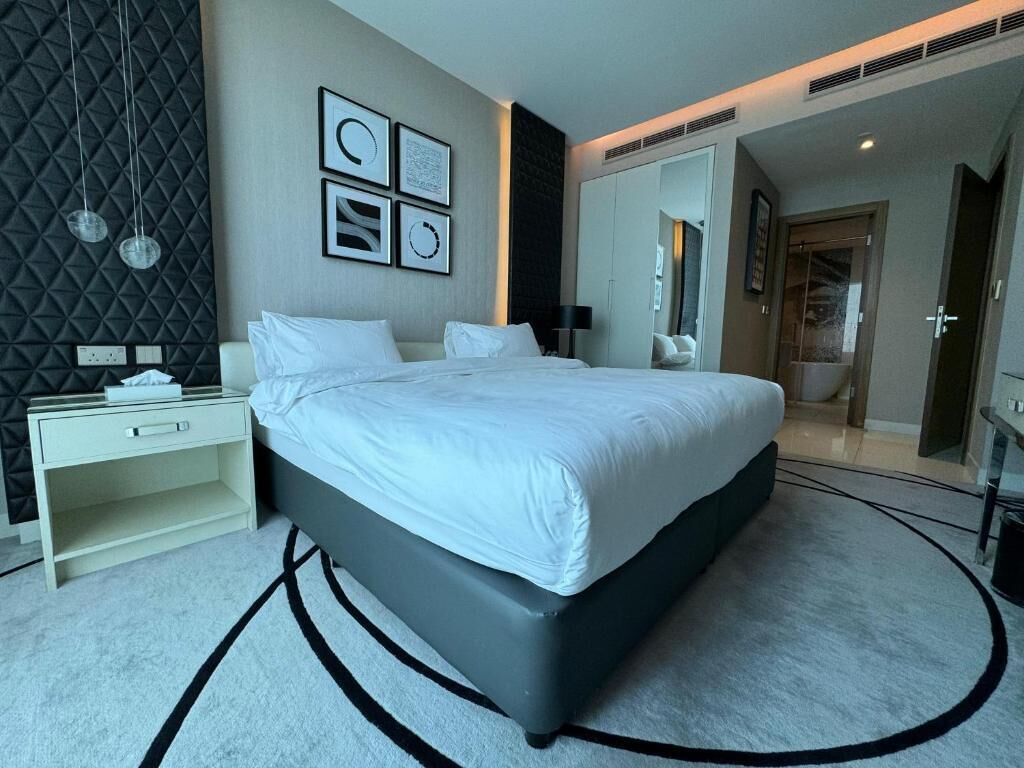 A modern bedroom with a large bed, a bedside table, a wardrobe, and a mirror.
