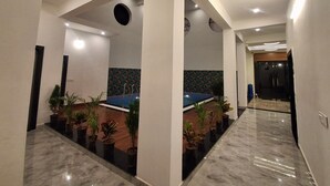 A modern hotel corridor with marble flooring, potted plants, and a blue seating area. - Hotel Aries Pushkar (Pushkar)