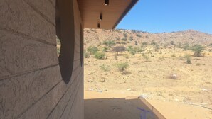 A view from a building with a large circular window, looking out to a dry, hilly landscape with sparse vegetation and scattered trees. - Hotel Aries Pushkar (Pushkar)