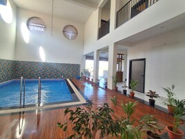 Una piscina interior con suelo de madera, rodeada de plantas en macetas, y una pared decorativa con diseño de hojas.