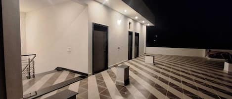 A modern building exterior at night with a tiled terrace, a staircase, and a door.