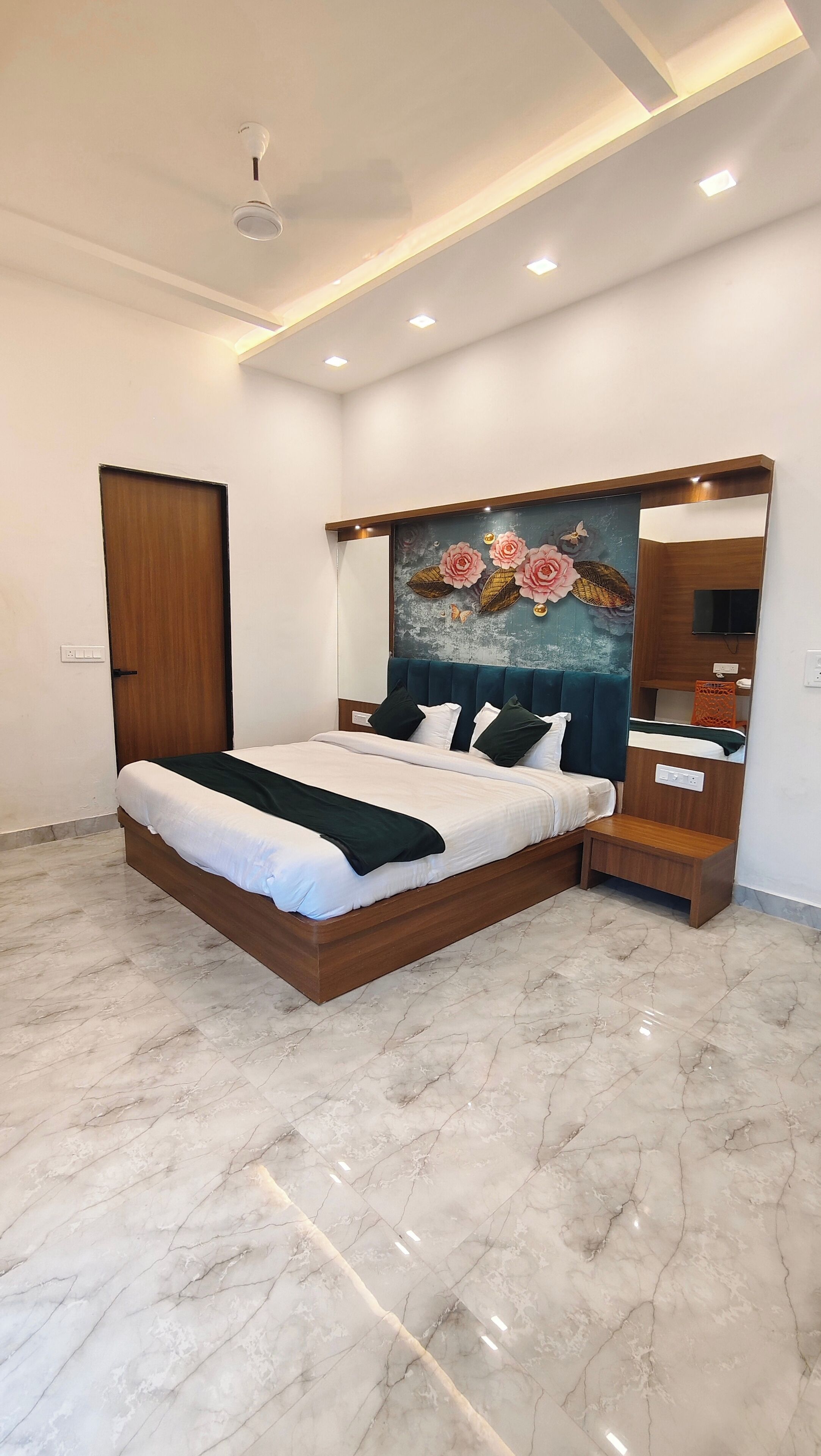 A modern bedroom with a large bed, a wooden headboard, a decorative wall painting, a mirror, and a built-in TV shelf.