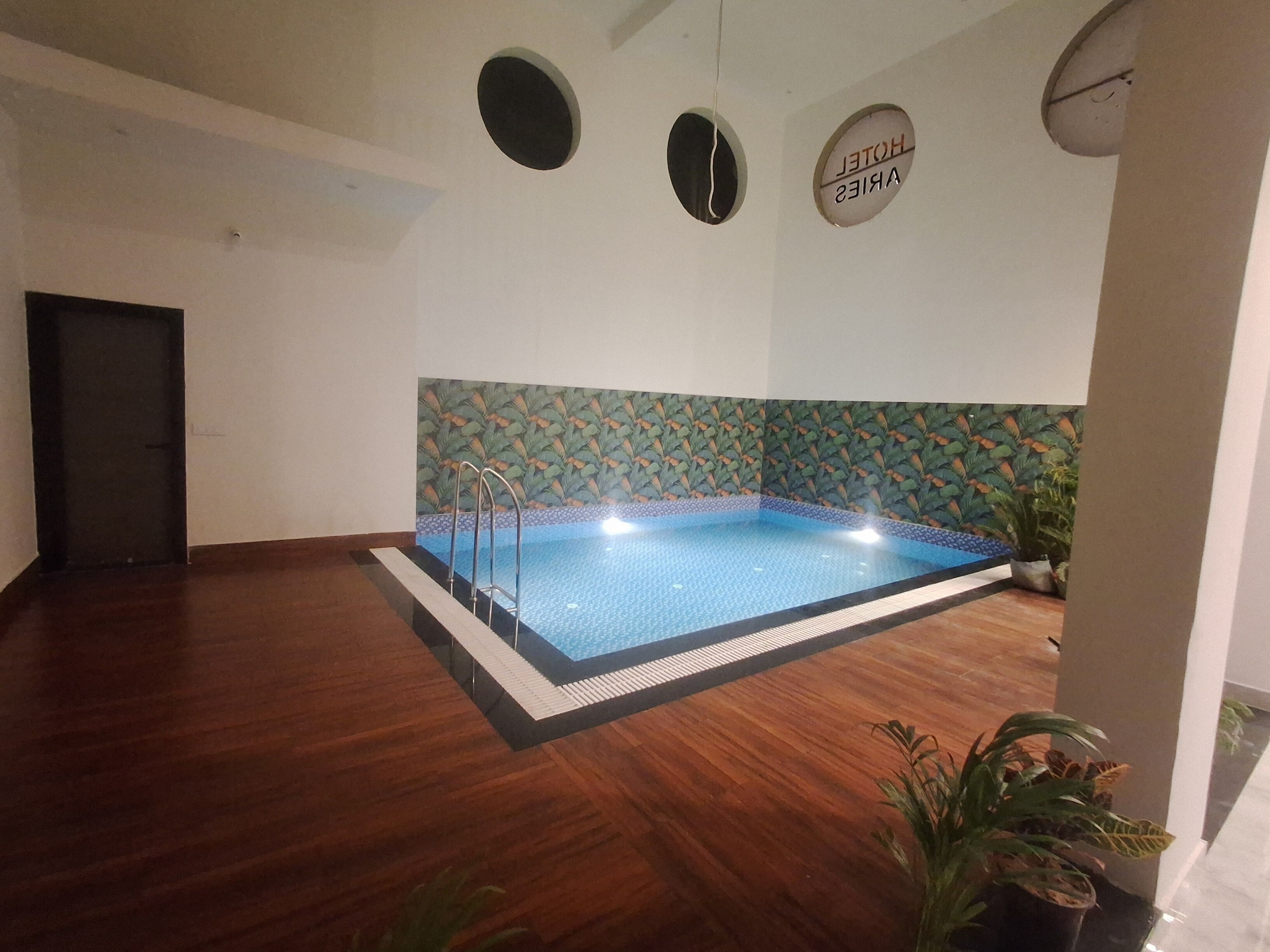 A swimming pool with a tiled edge, surrounded by a wooden floor, and a decorative wall with a leaf pattern.