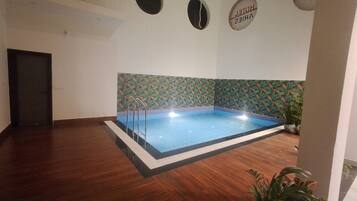 Una piscina con borde de azulejos, rodeada de un piso de madera y una pared decorativa con diseño de hojas.