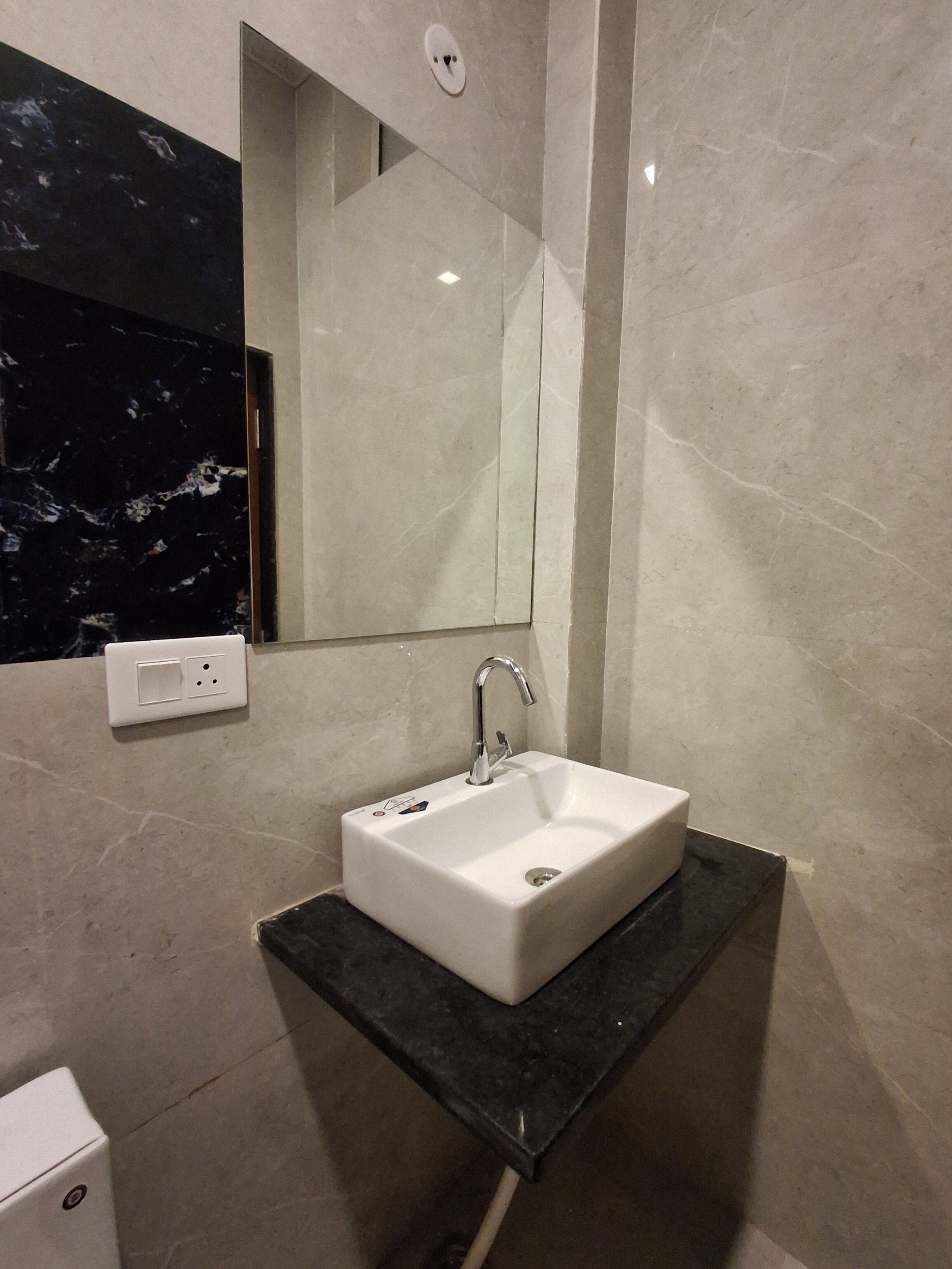 Un baño con lavamanos blanco, un espejo y encimera negra.