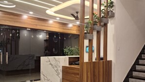 A modern reception desk with a marble top, wooden accents, and a ceiling with recessed lighting and a fan. - Hotel Aries Pushkar (Pushkar)