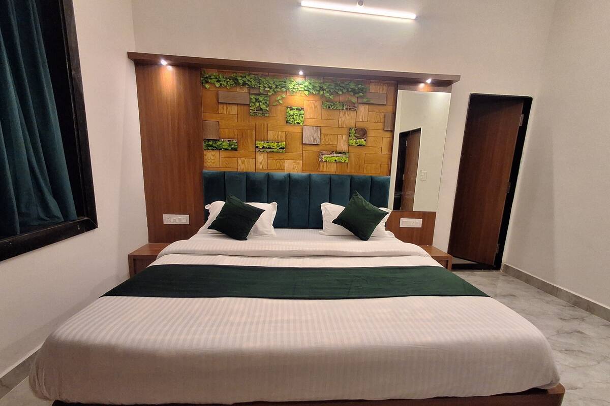 A neatly made bed with a wooden headboard, a green throw blanket, and two pillows.