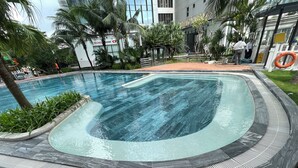 A swimming pool with a curved edge, surrounded by a tiled deck and palm trees. - Saturn- Vinhomes Skylake Apartment (Hanoi)