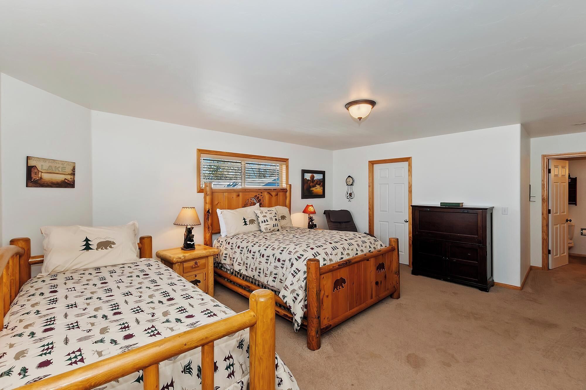 A bedroom with two beds, a wooden headboard, a nightstand with a lamp, a wall clock, and a framed picture.