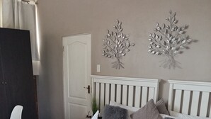 Een net opgemaakt bed met een handdoek gevouwen in de vorm van een zwaan, een wit hoofdeinde en twee decoratieve takken aan de muur.