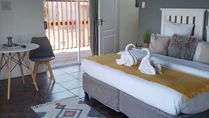 Een slaapkamer met een bed, een klein tafeltje met een stoel, een balkon met een houten hek en een deur.