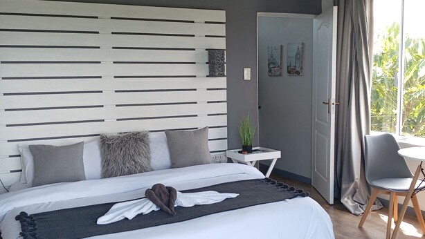 Een moderne slaapkamer met een groot bed, een nachtkastje, een stoel en uitzicht op groen.