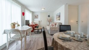 Un salón amplio y bien iluminado con una mesa de comedor preparada para cuatro personas, un sofá y una mesa de centro.