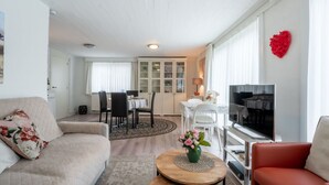 Una sala de estar con sofá, un sillón rojo, una mesa de centro, televisor y un comedor con mesa y sillas.