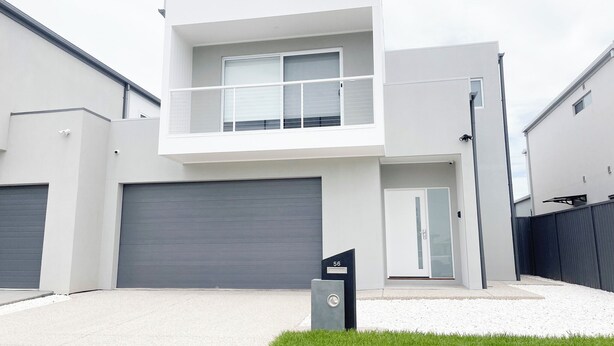 Une maison moderne à deux étages, avec une porte de garage grise, un petit balcon et une boîte aux lettres.
