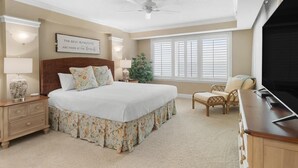 A bedroom with a large bed, a ceiling fan, a window with blinds, a nightstand with a lamp, and a television. - Oceanfront 3 Bdrm Getaway to the Beach Sleeps 6 (Pawleys Island)