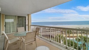 A balcony with a table and chairs, overlooking a beach and a pool. - Oceanfront 3 Bdrm Getaway to the Beach Sleeps 6 (Pawleys Island)
