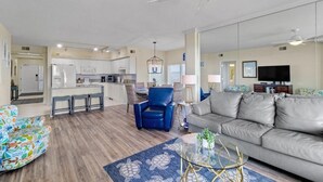 Un salon moderne avec un canapé, un fauteuil bleu, une table basse en verre et un tapis à motifs.