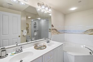 Une salle de bain avec un grand miroir, deux lavabos, une baignoire et une douche.