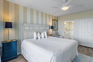 Une chambre avec un grand lit, deux tables de chevet, un ventilateur de plafond et une porte donnant sur une salle de bain.