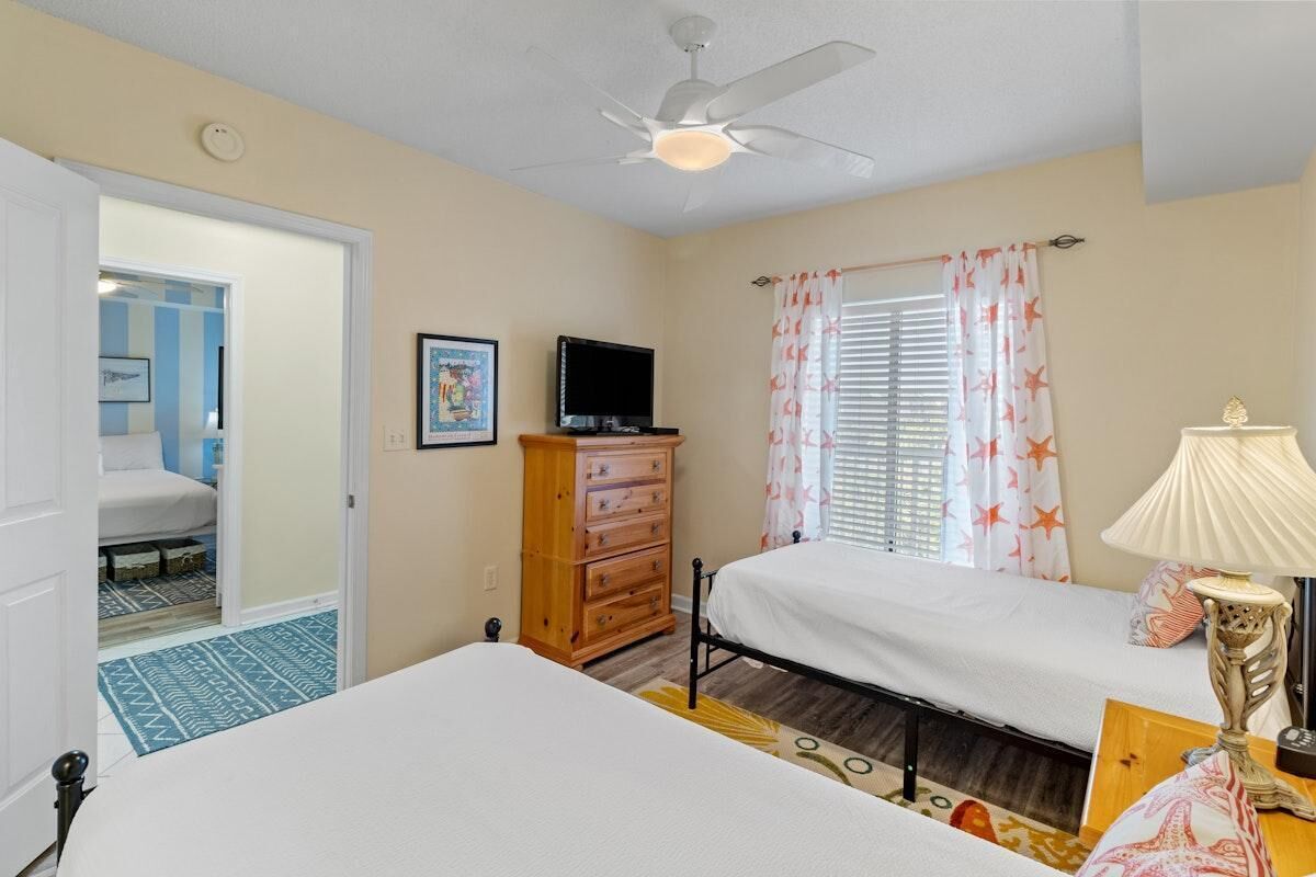 A bedroom with two beds, a ceiling fan, a TV, and a dresser.
