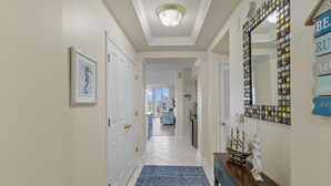 Un couloir avec un tapis bleu à motifs, une console en bois sur laquelle est posé un modèle de bateau, et un miroir avec un cadre en mosaïque.