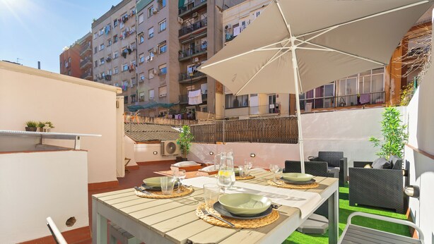 An outdoor dining area with a table set for four, surrounded by wicker chairs and a large umbrella.