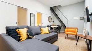 A modern living room with a grey sectional sofa, an orange armchair, and a staircase leading to an upper floor.