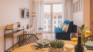 A modern living room with a blue sofa, dining table with chairs, and a large window with curtains. - Laguna Basen SPA Przy pla y Gara Wifi (Mielno)