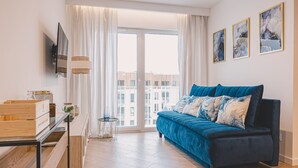 A modern living room with a blue sofa, a TV mounted on the wall, and a large window with curtains. - Laguna Basen SPA Przy pla y Gara Wifi (Mielno)