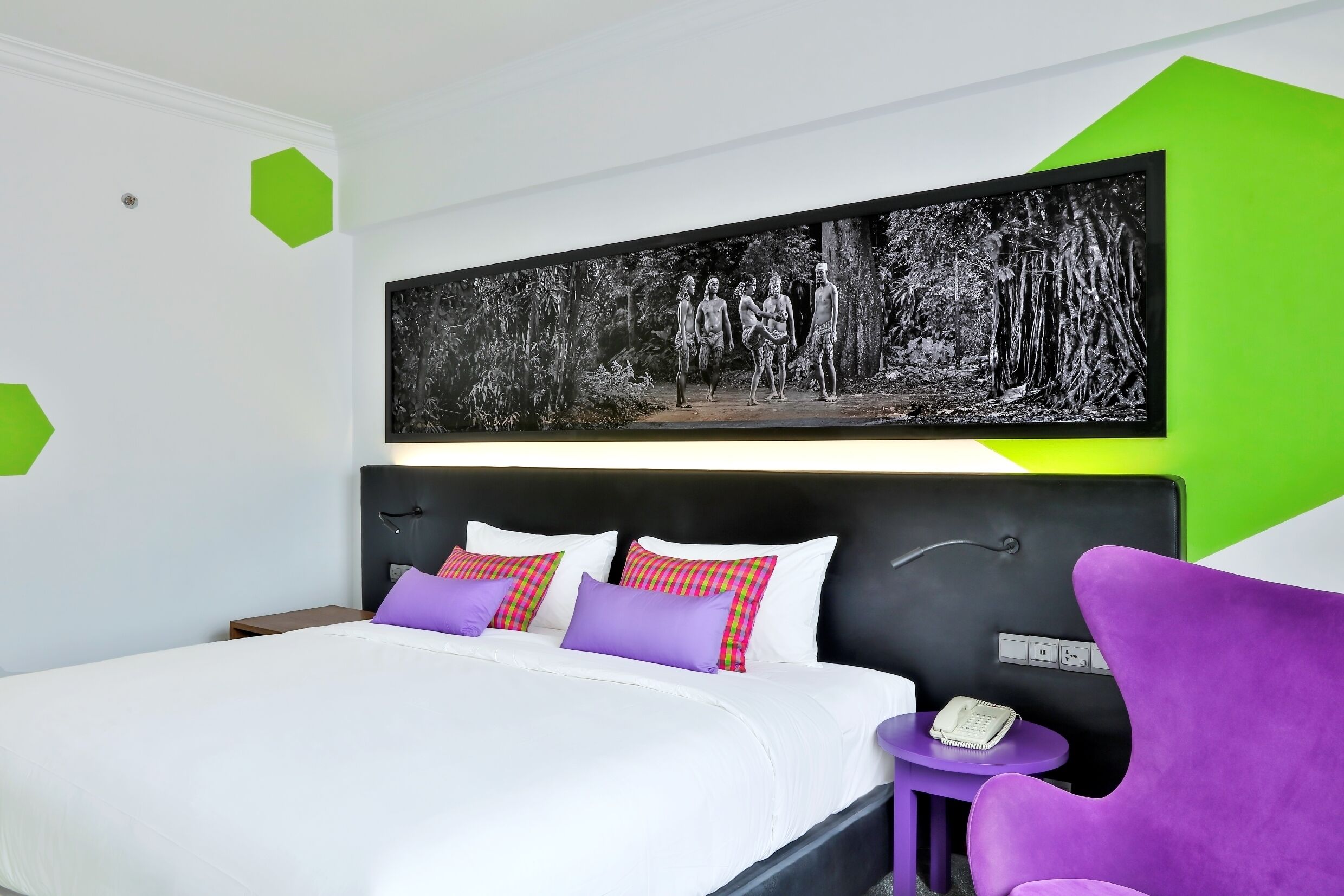 A modern hotel room with a large bed, a headboard with a built-in phone, and a wall-mounted artwork depicting a forest scene.